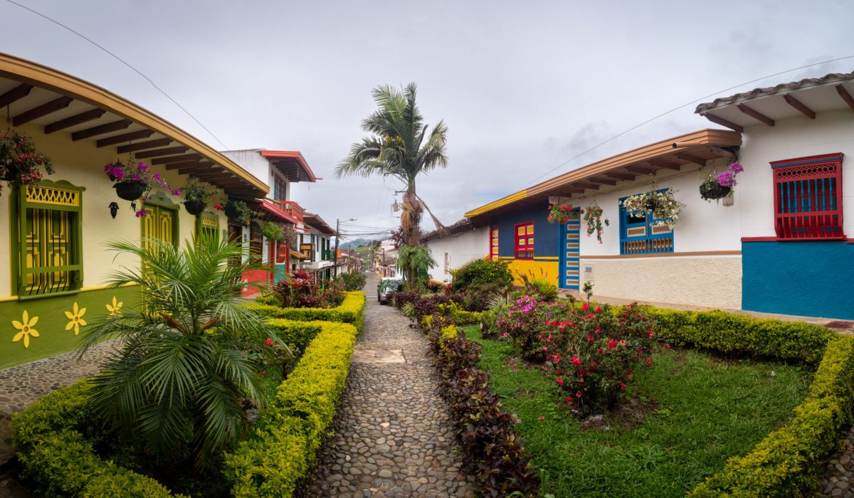Jerico, Antioquia, Colombia - April 5 2022: Beautiful Gardens with Bushes and Flowers in Colonial Street with Colourful Houses and Palm Tree in the Background
